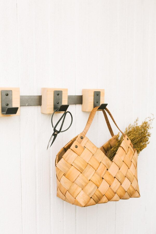 a weaved basket bag hanging on a metal hook rack next to scissors