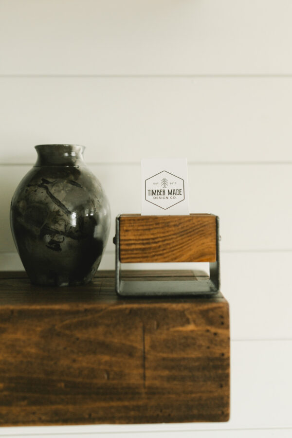 a small wooden business card holder in dark walnut sitting on a shelf next to a vase