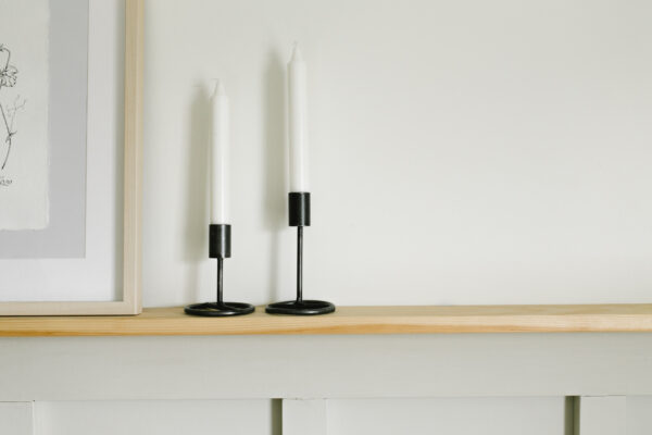 two metal candlestick holders on a wood shelf