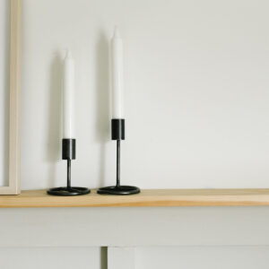 two metal candlestick holders on a wood shelf