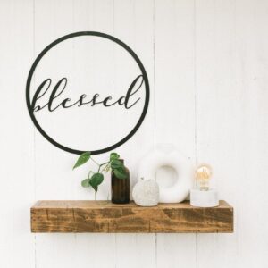 round metal sign with blessed in the middle - hanging above a small wooden shelf