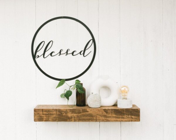 round metal sign with blessed in the middle - hanging above a small wooden shelf