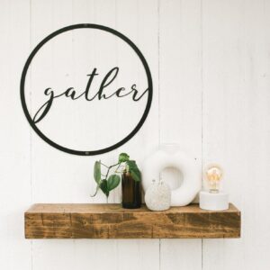 round metal sign with the word gather in the middle - hanging over a small wooden shelf